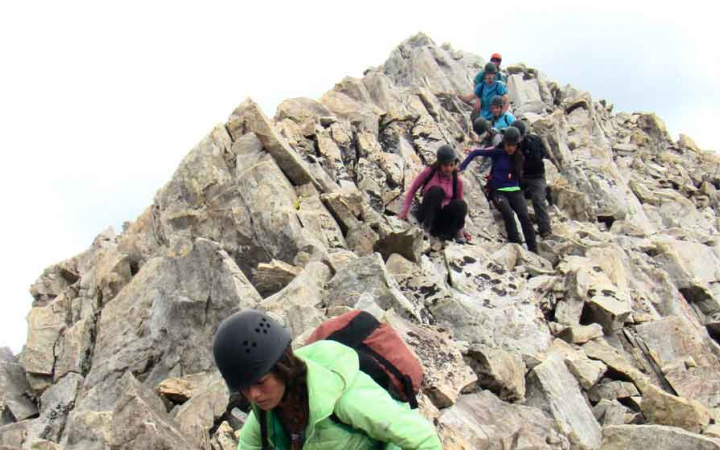A group of students wearing helmets hike downwards from a rocky incline